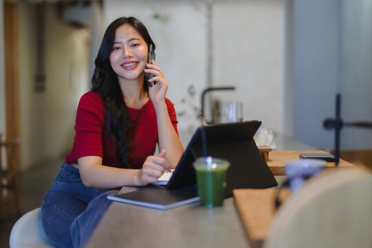Young Asian woman talking on smartphone smiling at coffee shop