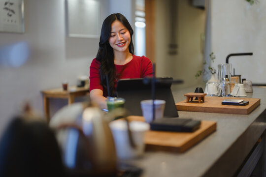 Young Asian woman smiling using tablet in modern cafe