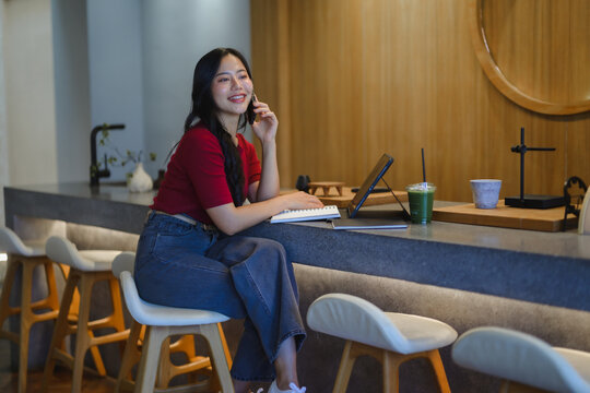 Young Asian woman talking on phone enjoying cafe environment
