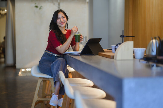Young Asian woman working at coffee shop table drinking green juice