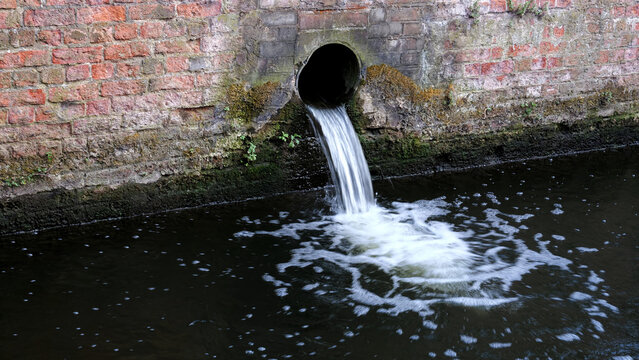 Wastewater discharge pipe, water pollution, drain pipe pouring sewage into river, ecological disaster, industrial waste drainage from old brick wall