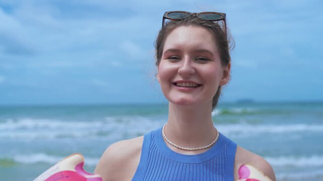 Cheerful woman with a pink floatie fully embracing a digital detox and the freedom of a relaxing summer weekend getaway by the ocean.