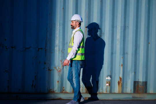 Male walk. Handsome caucasian male dock foreman worker in white hard hat helmet and high-visibility vest walking in Shipping Cargo Container Terminal Depot