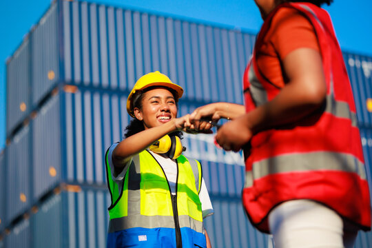 Unity and teamwork concept. Hand shake African woman logistics workers in hardhat helmet and high visibility safety gear at shipping container yard