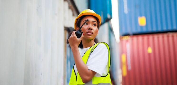 Black female dock worker control loading containers box from cargo at warehouse container yard. Marine and carrier insurance concept. cargo shipping container box in logistic shipping yard