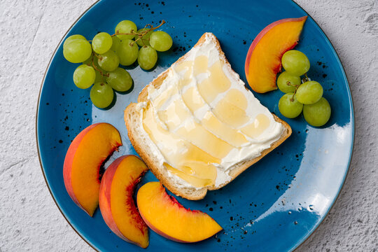 Healthy breakfast plate with toast topped with cream cheese and honey, served with fresh grapes and peach slices