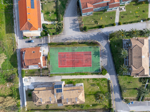 Aerial Top Down View of Green and Red Tennis Court Surrounded by Resort Villas in Corfu Greece