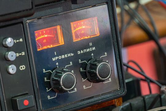 Vintage audio mixing console featuring analog vu meters, recording level text, rotary knobs, dark tones, red backlight contrast, well-organized cables, professional environment