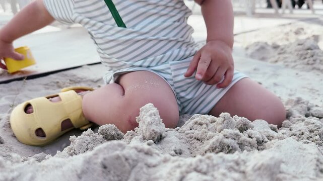 Toddler playing in beach sand with yellow cup