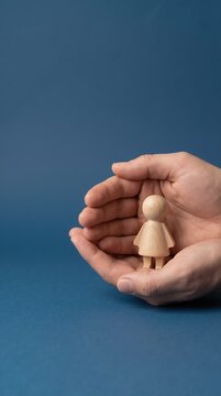 Vertical photo of hands protecting wooden female figure. Concept of life insurance and family safety. Nurturing and care for women. Support and security