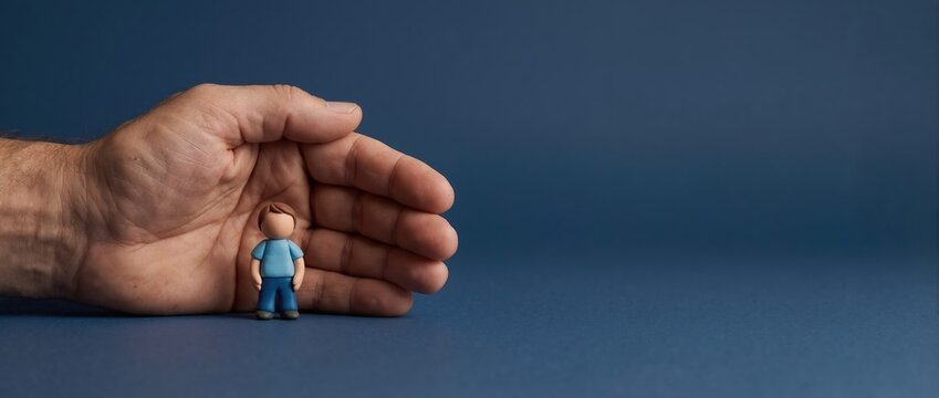 Human hand protecting small boy figure on blue background. Child safety and family insurance concept. Social welfare and support for children. Copy space for text