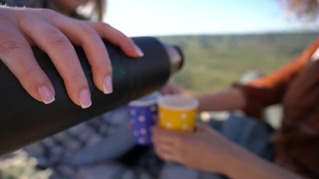 Picnic travel leisure two women pouring tea from thermos on hilltop field during sunset for summer nature vacation activity