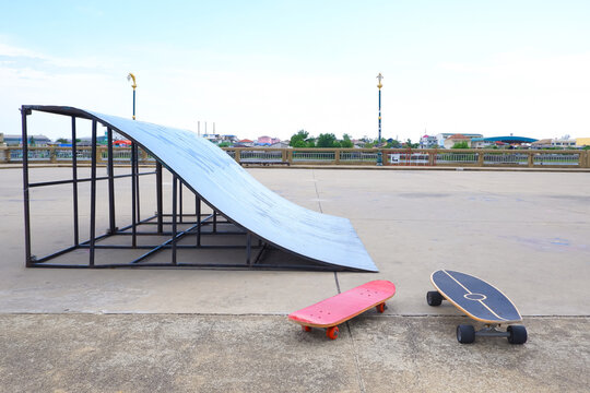 Outdoor concrete skatepark with skate ramp and two skateboards against city skyline view