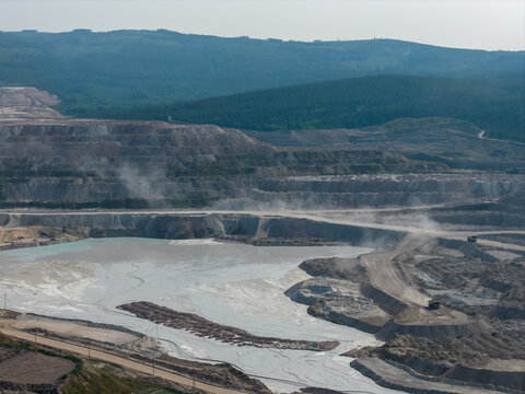 Open Pit Mine And Industrial Quarry Landscape With Dump Trucks Against Forested Hills In British Columbia Canada