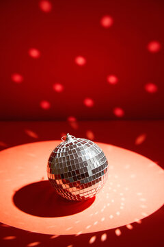 Shiny disco ball, also known as mirror ball, on a red surface with scattered light reflections. Disco ball decoration with light reflections on vibrant red background
