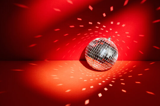 Shiny disco ball, also known as mirror ball, on a red surface with scattered light reflections. Disco ball decoration with light reflections on vibrant red background