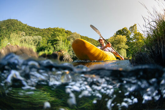 Whitewater kayaking in a river surrounded by green trees and hills on a sunny day