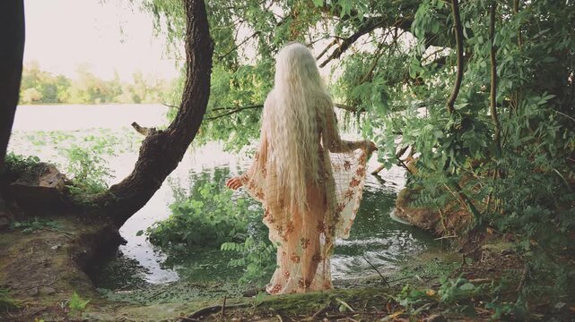 silhouette fantasy woman river nymph walking in swamp green water. happy fairy girl back rear view enjoys beauty wild nature tree. Elf goddess back view wet beige golden color dress. long blonde hair.