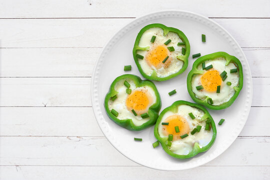 Healthy breakfast concept with eggs in green peppers on a plate. Above view over a white wood table background.
