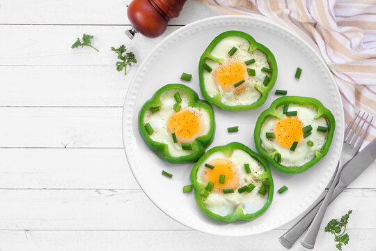 Healthy breakfast concept with eggs in green peppers on a plate. Top view over a white wood table background with copy space.