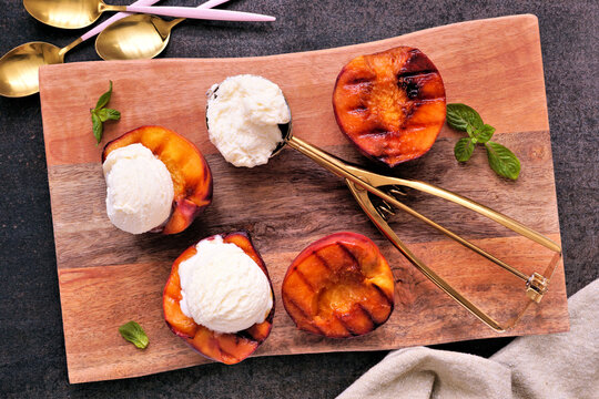 Sweet grilled peaches with vanilla ice cream on a wood platter. Overhead view table scene on a dark background.