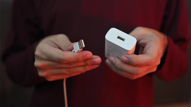 Hands holding a coiled phone charging cable against