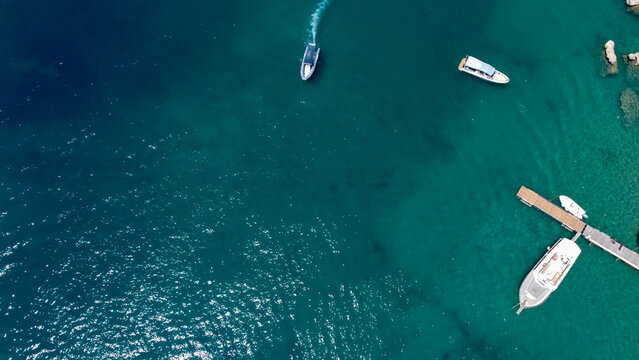 Top-down aerial drone view of a small boat moving smoothly across crystal clear blue ocean water, leaving white waves behind. Luxury tropical travel and summer vacation concept. Gozo, Mgarr, Malta.