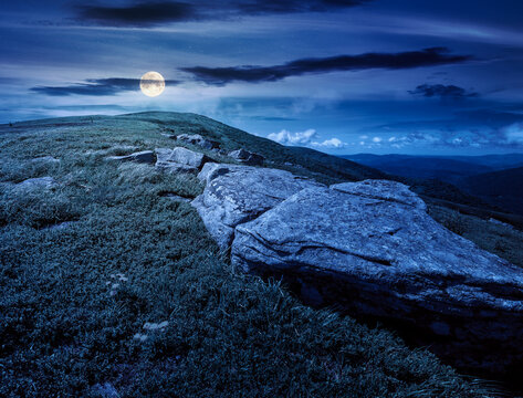 carpathian mountain landscape on summer night. fantasy view of a grassy alpine meadow. full moon over rock and yellow herbs on the hill. mysterious mountain weather with cloudy sky