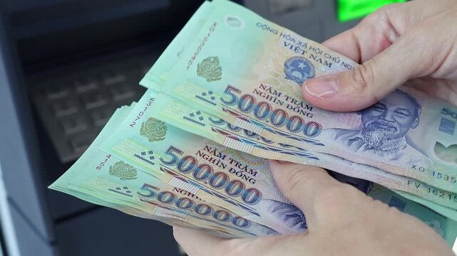 Close up view of woman hands counting Vietnamese dong banknotes (VND) in ATM. Concept of saving money for retirement, cash settlement, financial goals, success, literacy and income planning in Vietnam