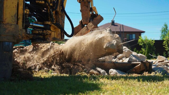 Heavy machinery with a jaws attachment demolishing concrete and creating a dust cloud, working on a renovation site with debris scattered on the ground