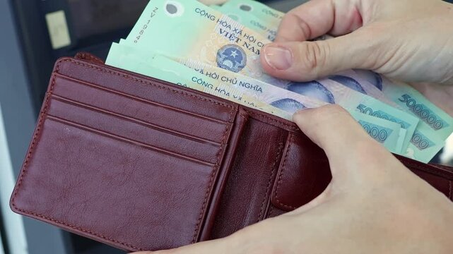 Close up view of woman hands, wallet and Vietnamese dong banknotes in ATM. Concept of saving money for retirement, cash settlement, financial goals, success, literacy and income planning in Vietnam.