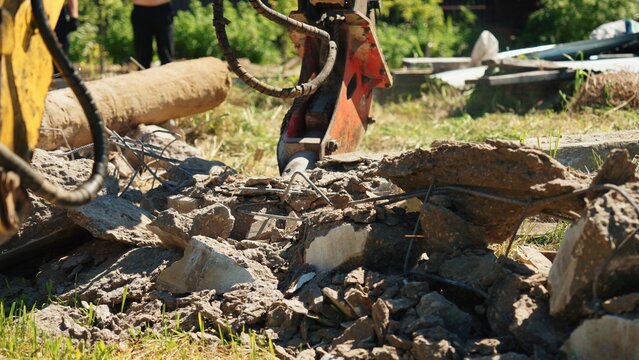 Heavy machinery with a hydraulic hammer breaking down concrete pieces and rebar on a construction site, creating rubble and demonstrating demolition in progress
