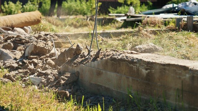 Close-up of exposed reinforcing steel protruding from a demolished reinforced concrete foundation with broken rubble and dust during residential demolition, showing structural removal