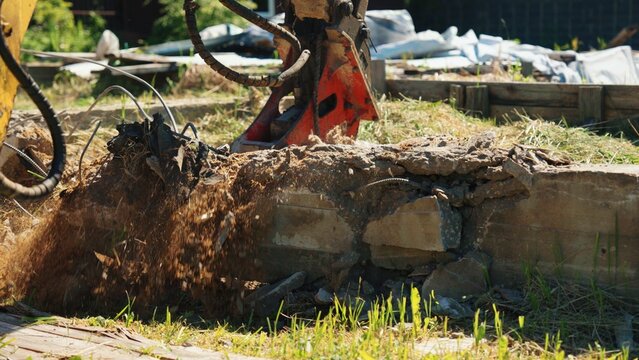 Heavy equipment attachment breaking apart a concrete foundation, creating dust and debris during a building demolition or renovation project