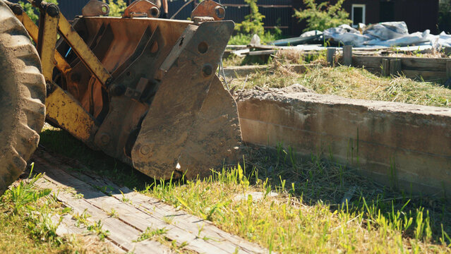 Yellow backhoe bucket and tire of heavy equipment moving earth at a construction site, preparing the ground for building
