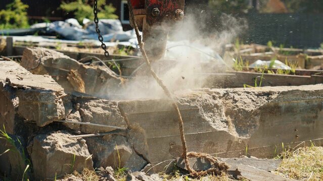 Close-up of a hydraulic breaker impacting a reinforced concrete foundation, creating a large dust cloud during residential demolition, highlighting structural removal, heavy machinery