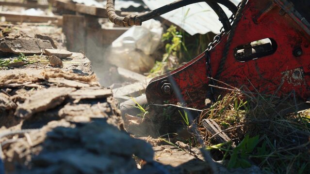 Demolition machine breaking concrete structure with its hydraulic hammer attachment at a construction site, creating dust and debris from the impact