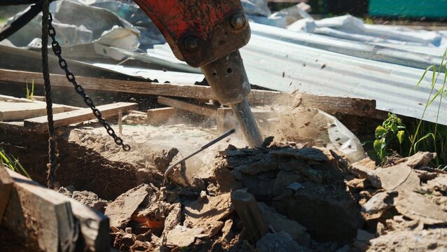 Hydraulic breaker attachment on an excavator crushing concrete and rebar during demolition work at a construction site, creating dust and debris