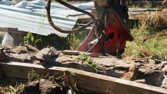 Close-up of a red demolition attachment beside broken concrete, timber and exposed debris during clearance of an old outdoor structure.