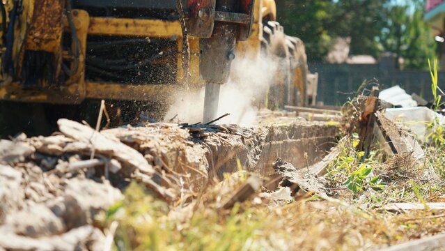 Heavy machinery featuring a hydraulic breaker attachment is actively pulverizing a concrete structure, creating dust and debris during a demolition or renovation project
