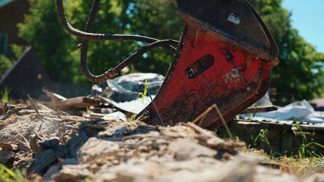 Heavy duty excavator attachment breaking up concrete and debris, creating dust and rubble in a demolition area on a sunny day