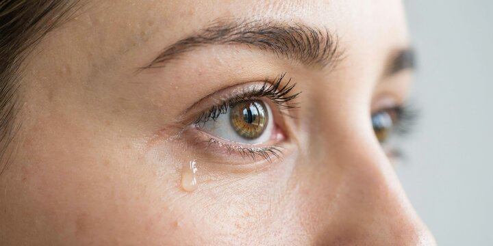 Close-up of a woman's eye with tear rolling down her cheek, conveying sadness and emotion.