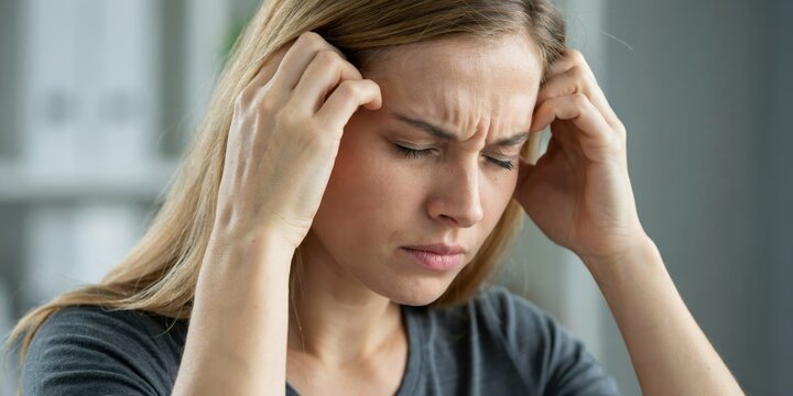 Stressed young woman holding head with both hands suffering from severe migraine pain.