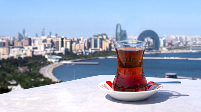Traditional Azerbaijani black tea served in an elegant armudu glass with a scenic Baku cityscape in the background, blending local culture with urban charm.
