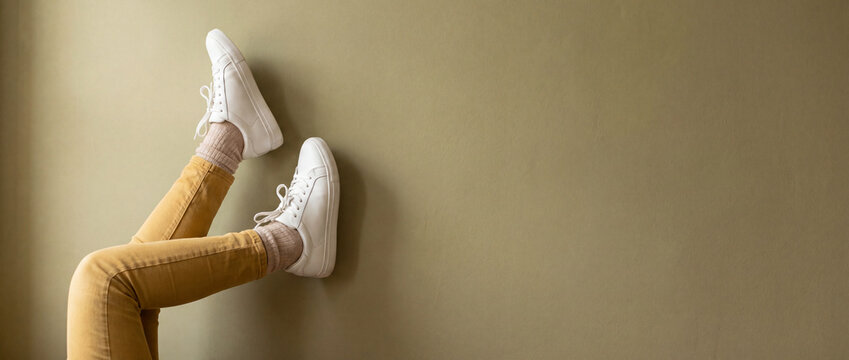 Legs in sneakers up on green wall, wearing yellow trousers and white leather shoes in a minimalist indoor setting, perfect for youth lifestyle, fashion advertising, and copy space design