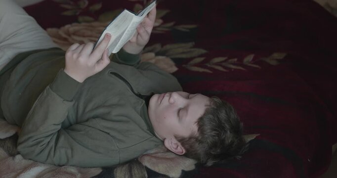 Caucasian Boy Kid Read Bible Book Lying on Bed in Bedroom. 4K 10-bit
