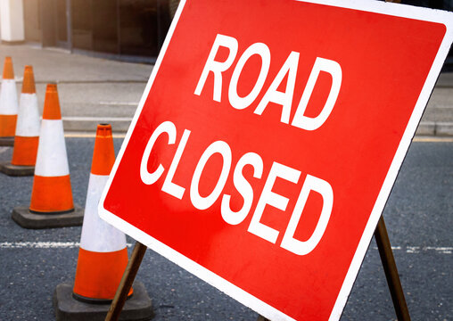 Road closed sign. Street block with car travel diversion signage and cones.