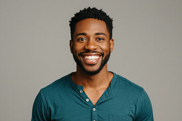 Obraz premium Portrait of young african american man with short haircut smiling at camera. Male person wearing casual teal henley shirt poses on neutral grey studio background. Happy guy with beard looks