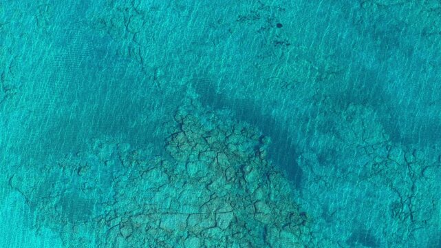 Overhead aerial drone view of crystal-clear turquoise water over a rocky reef seabed, Crete, Greece