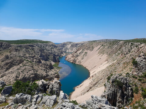 A stunning high angle view of the vibrant blue Zrmanja River canyon in Croatia, winding through steep rocky cliffs and rugged wilderness under a clear, bright summer sky.